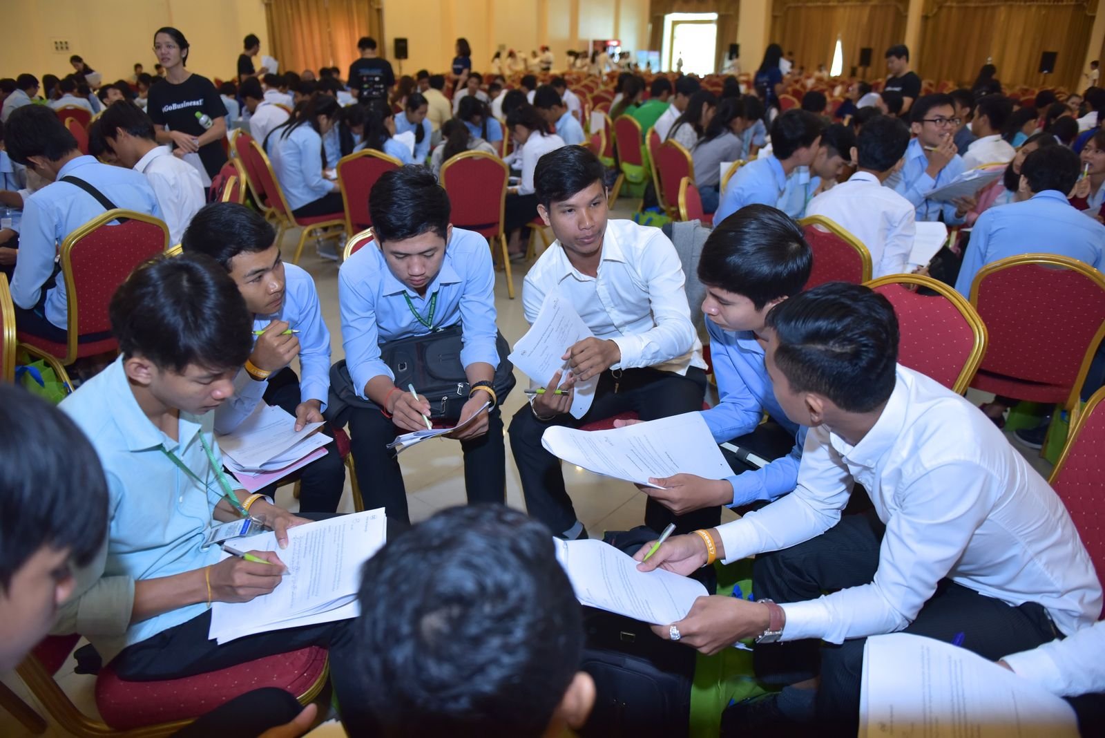 A very large hall of young participants, including Buddhist monks, working through R4B exercises in small groups